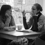 Black and white photo of Katharine sitting at a table, in conversation with a group of other people.