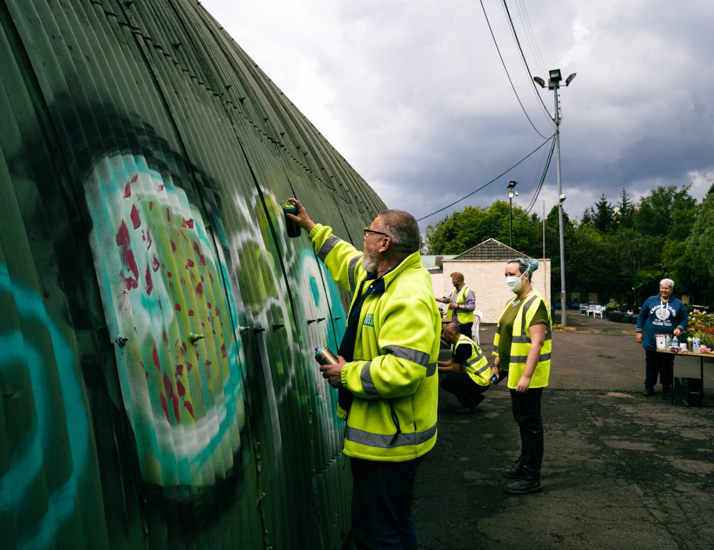 Participants in fluorescent yellow jackets paint a corrugated iron shed