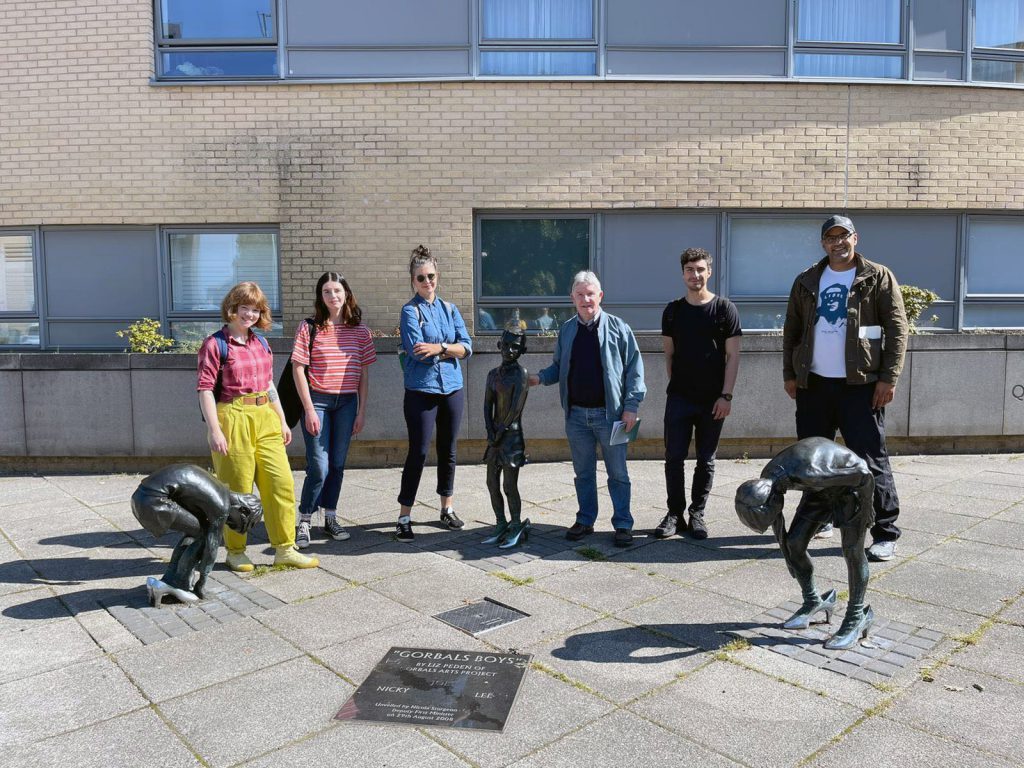 Street Level's six artists stand in the sunshine amidst an outdoor sculpture of three young boys titled 'Gorbals Boys'.