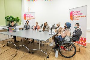 7 people sit around a table with microphone in front of them. There are Culture Collective banners behind them.