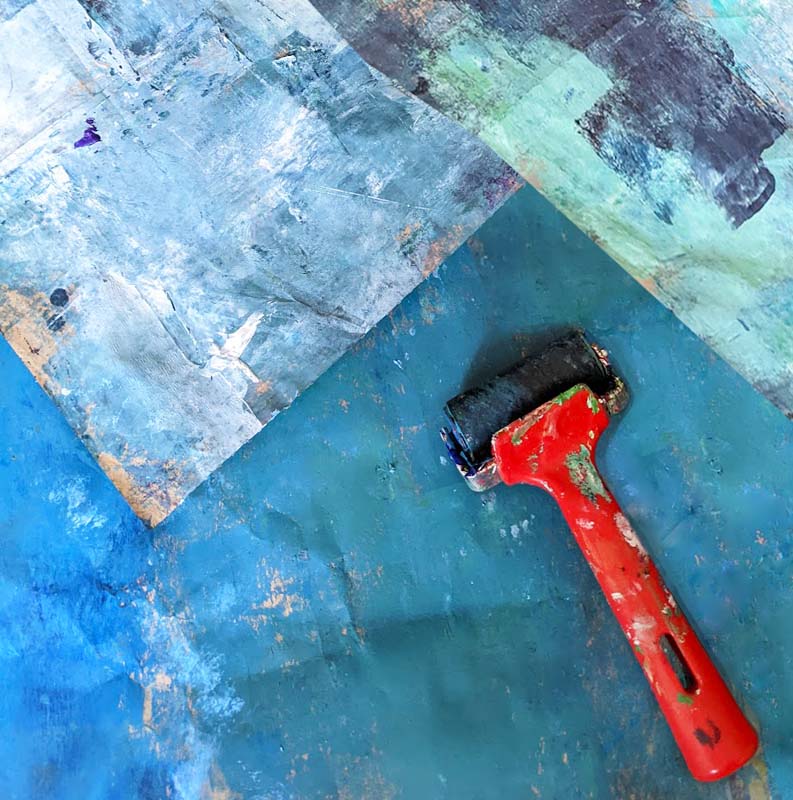 A photograph of an ink roller against a backdrop of recently inked wood in varying shades of blue.