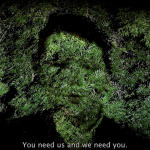 A video still, showing a boy's face screened onto the leaves of a mature tree. Captions at the bottom read "you need us and we need you"